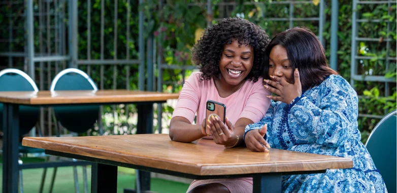 Two young women smiling while using a mobile phone together
